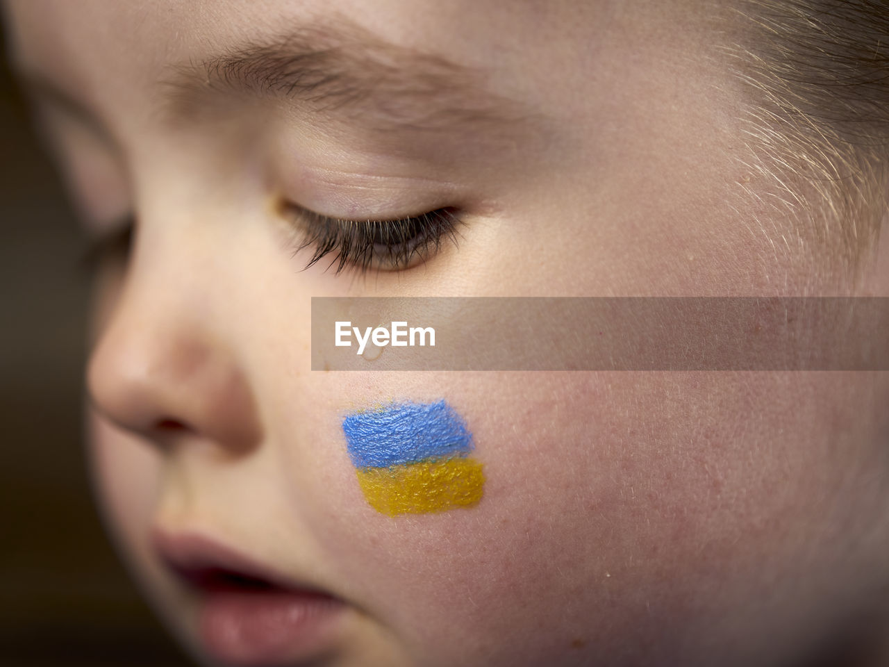 Child's crying with blue-yellow flag on cheek