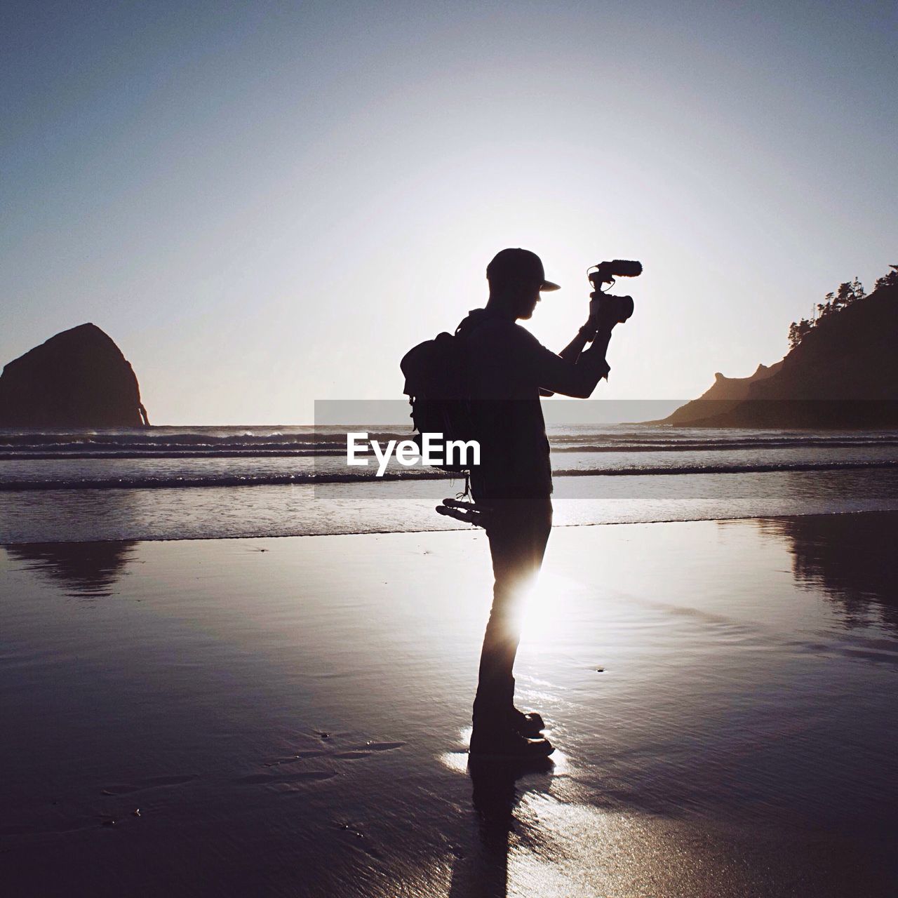 Side view of silhouette man video recording on beach during sunset