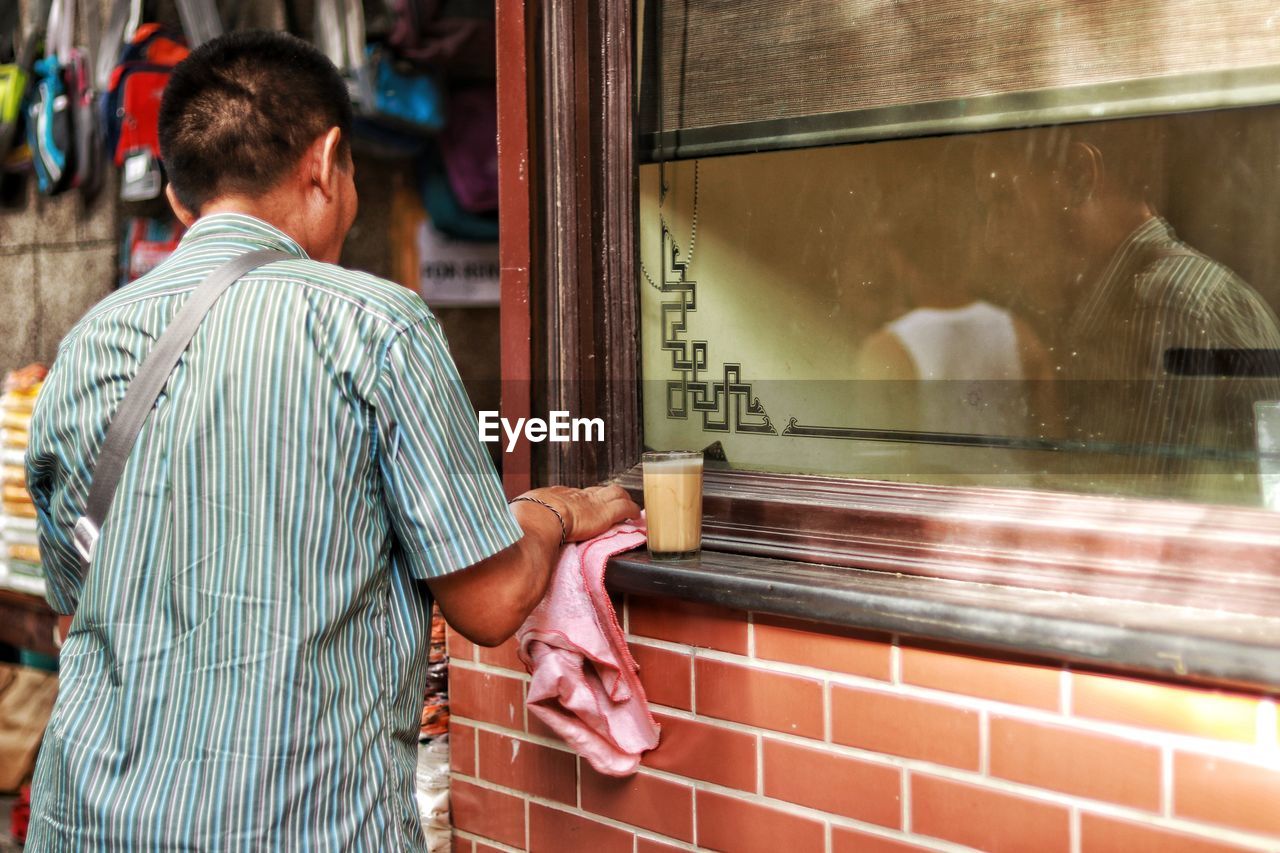 Rear view of man by drink on window sill