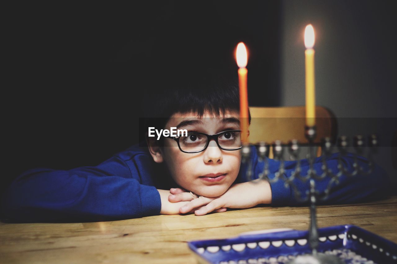 Boy wearing eyeglasses while looking at lit candles at home