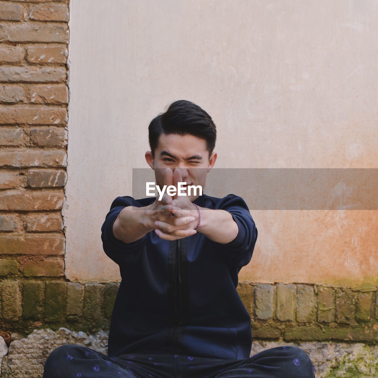 Young man sitting against  wall