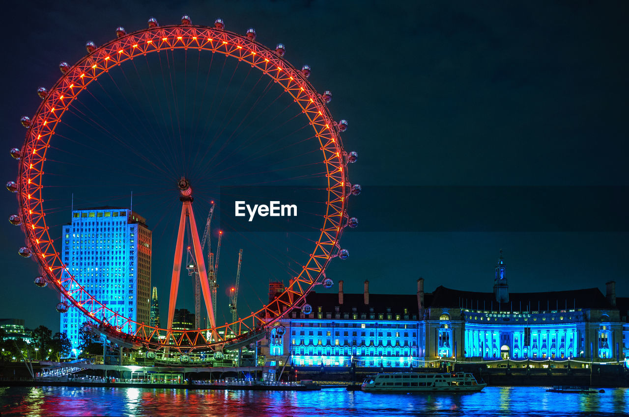 Illuminated millennium wheel and buildings against sky at night