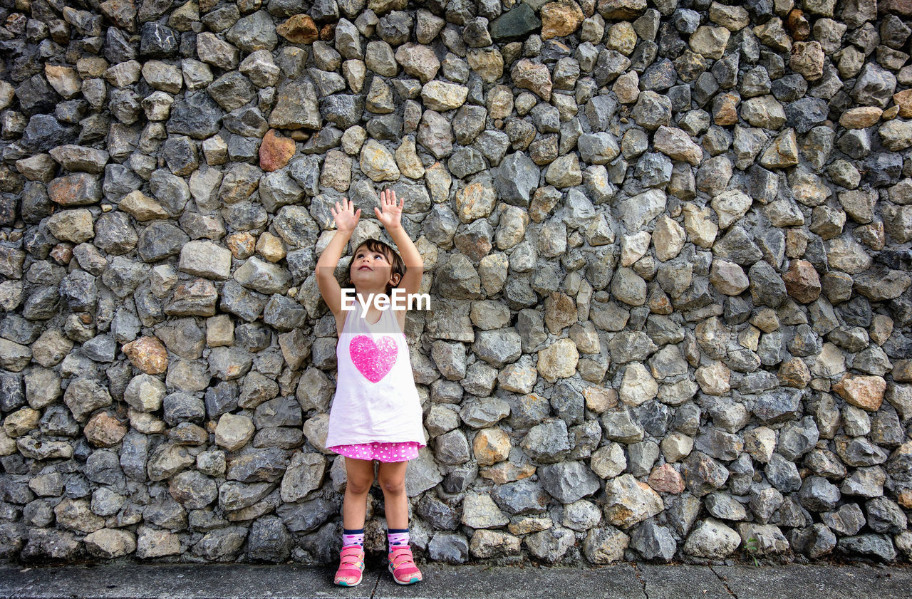 Cute girl standing on street against stone wall