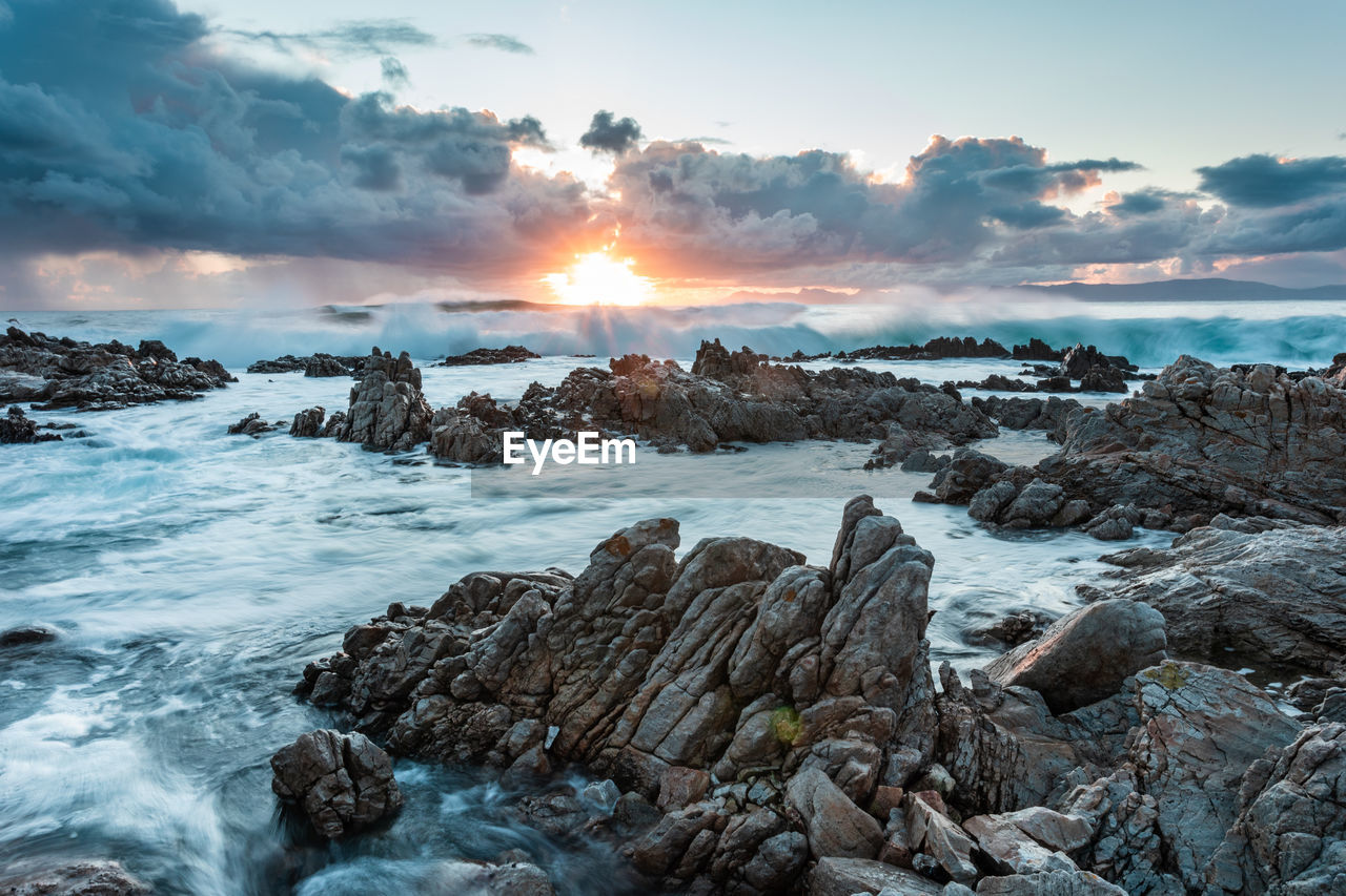 scenic view of rocks on beach against sky during sunset