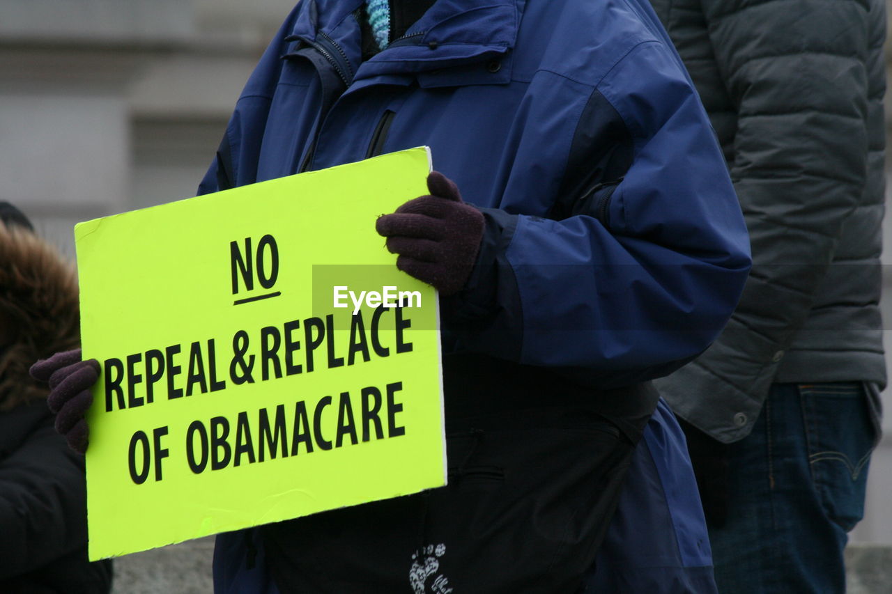 Midsection of protestor holding placard with text on street