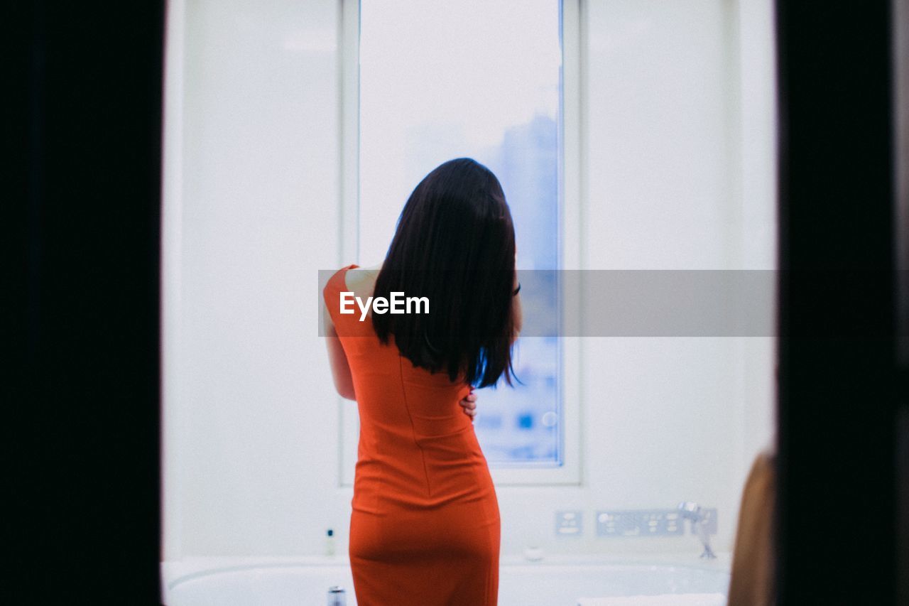 Rear view of woman standing against window