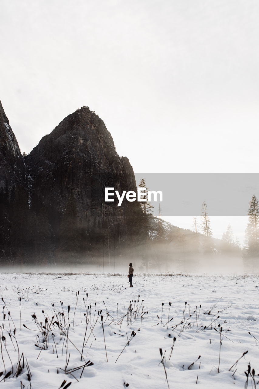 Distant unrecognizable person walking on breathtaking scenery of blizzard in winter in highland area on background of gray sky