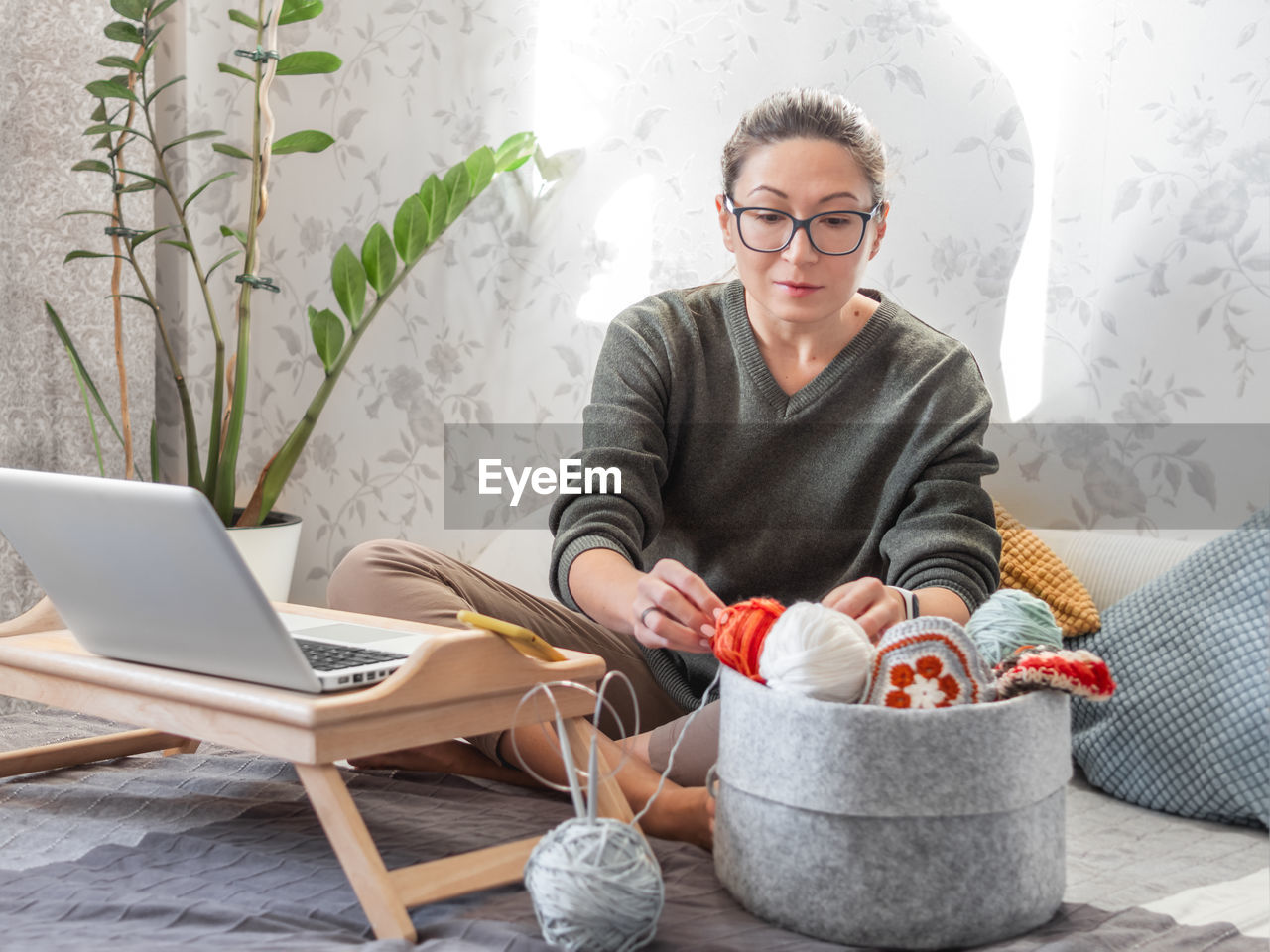 Woman chooses yarn for crocheting with movie on laptop.learn to knit from video lessons on internet.