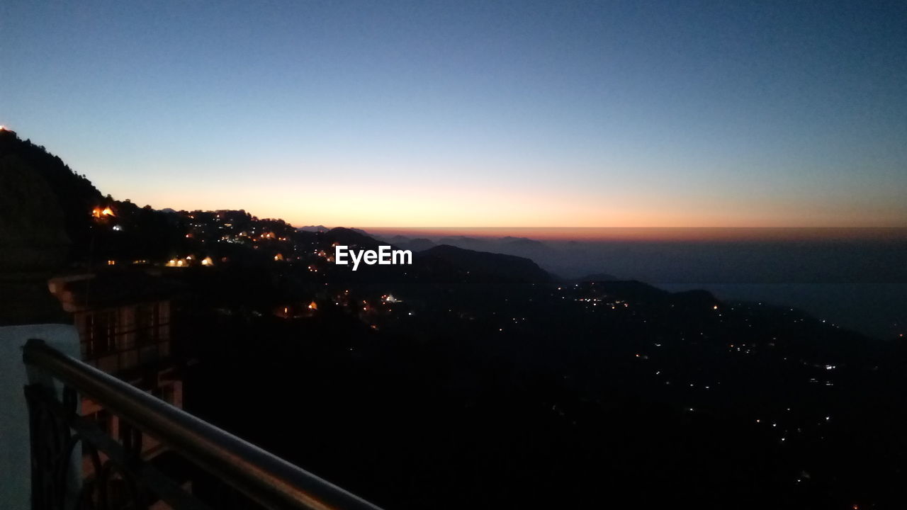 HIGH ANGLE VIEW OF ILLUMINATED CITYSCAPE AGAINST SKY AT SUNSET