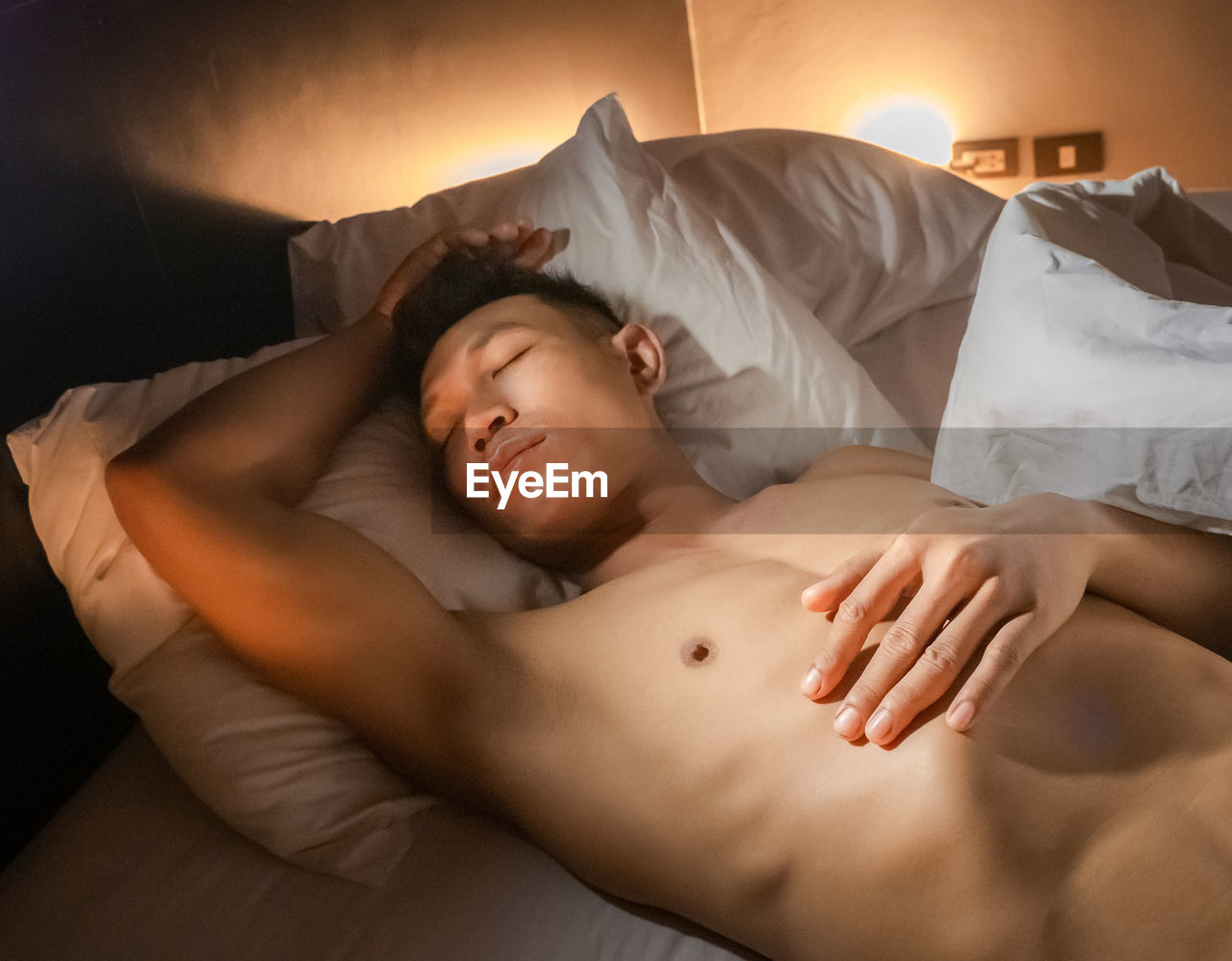 Young adult sleeping shirtless on the bed