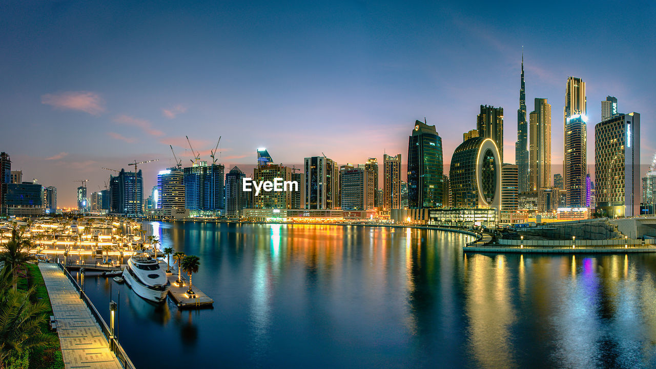 Illuminated buildings by river against sky in city