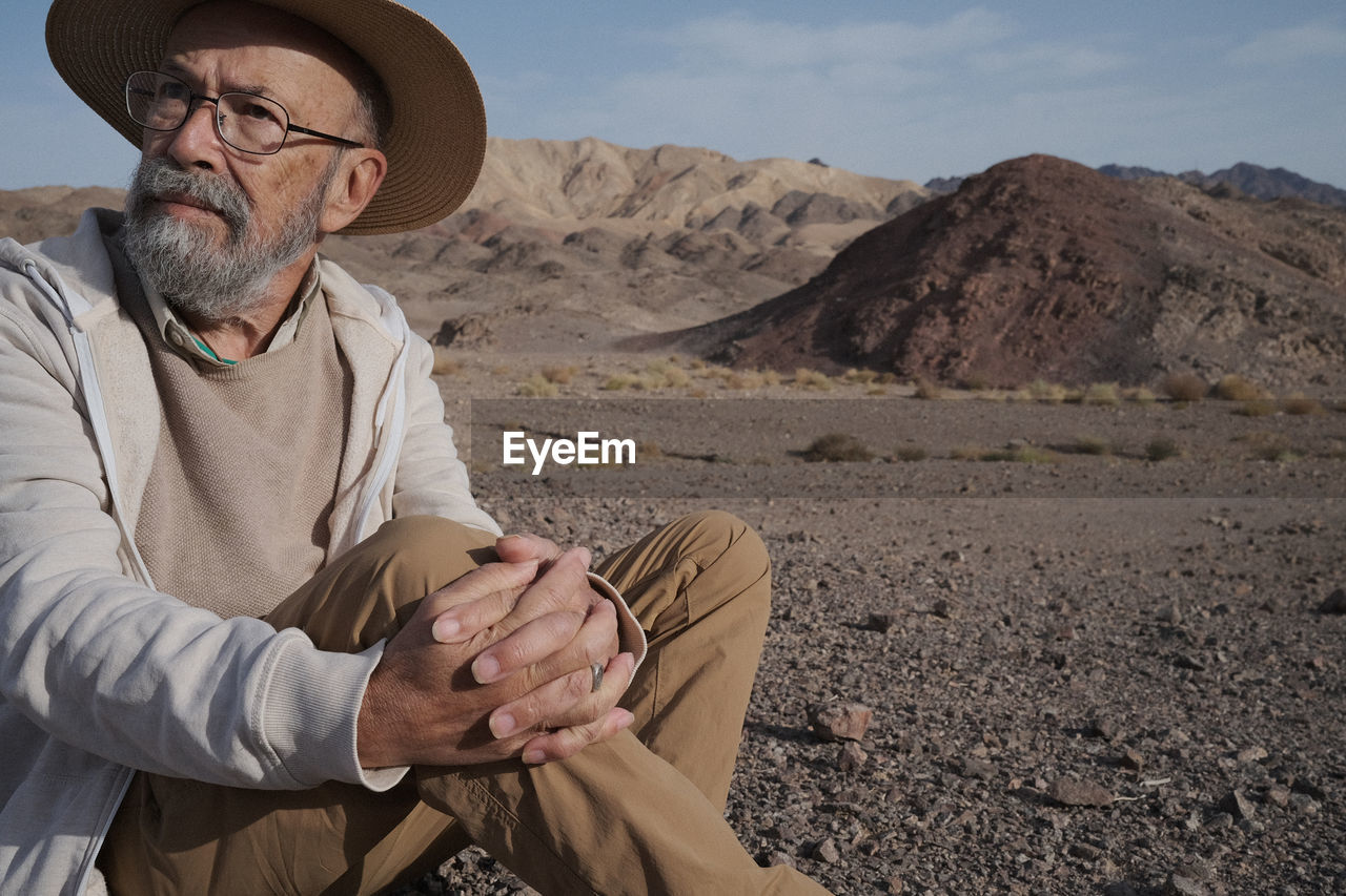 side view of man sitting on sand at desert