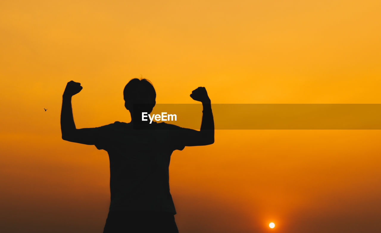 SILHOUETTE MAN WITH ARMS OUTSTRETCHED AGAINST ORANGE SKY