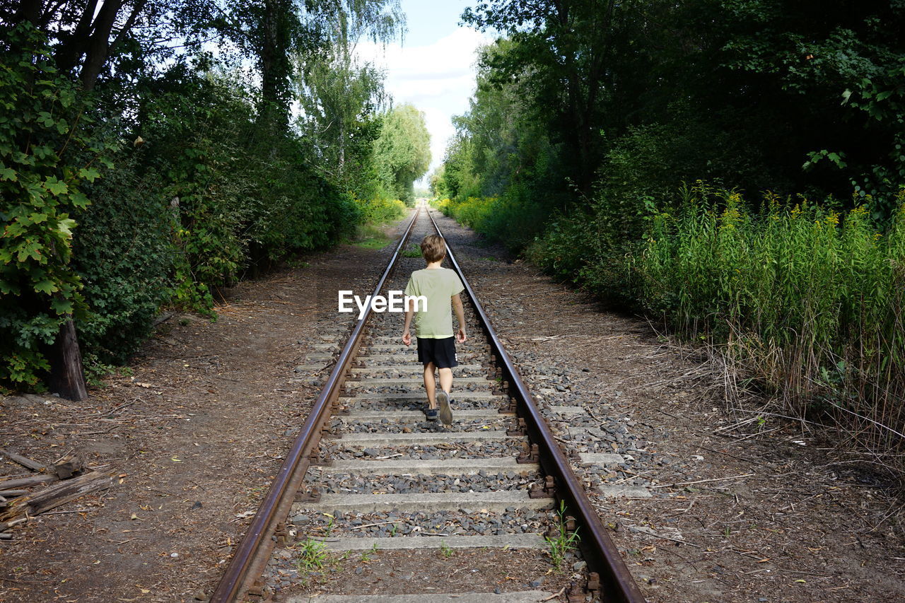 REAR VIEW OF PERSON WALKING ON RAILROAD TRACKS