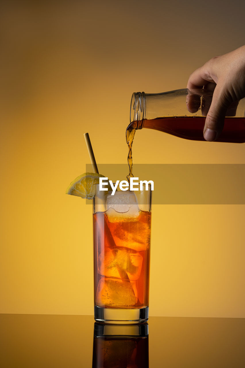 Close-up of hand holding drink against orange background