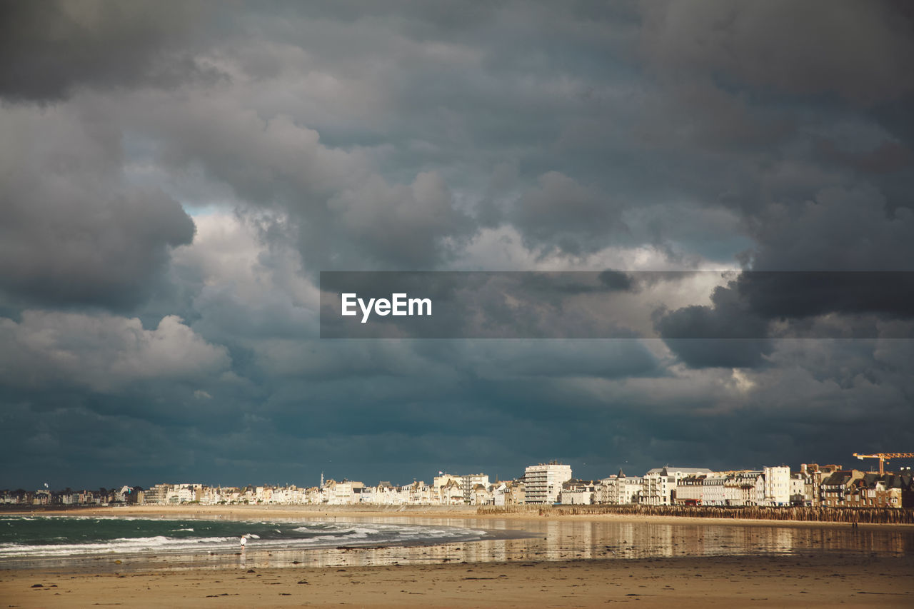 View of cityscape by sea against storm clouds