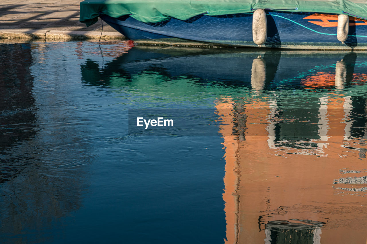 Boat moored in canal with reflections on water