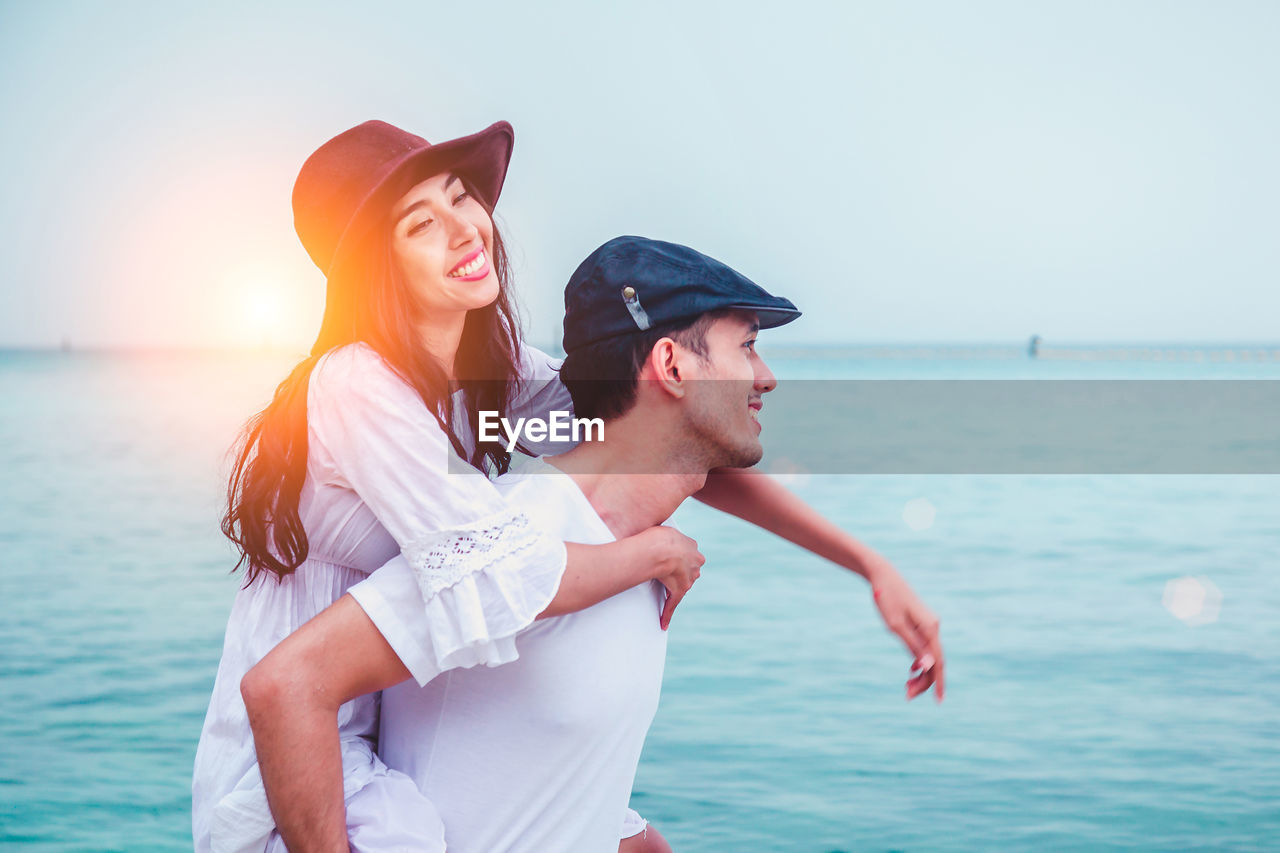 Smiling husband piggy backing wife while standing at beach