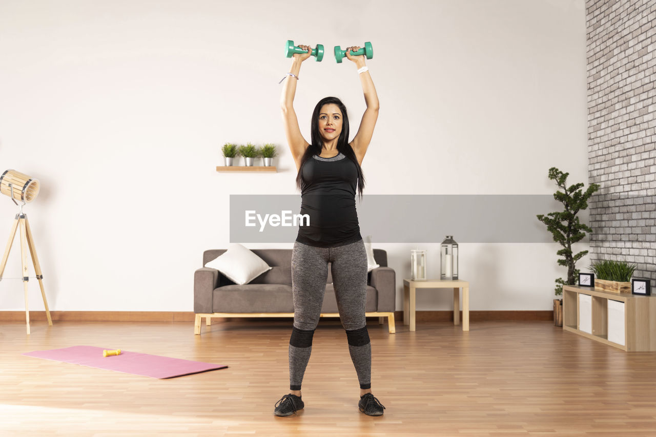 Pregnant woman exercising with dumbbells at home