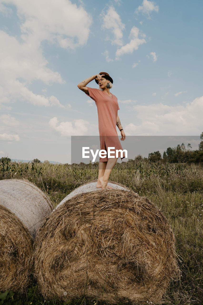 Full length of woman standing on hay bale against sky