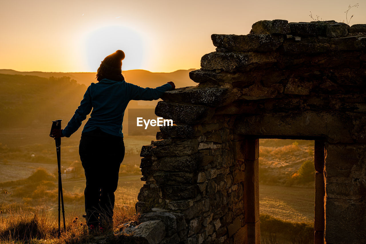 Rear view of man standing on rock against sky during sunrise