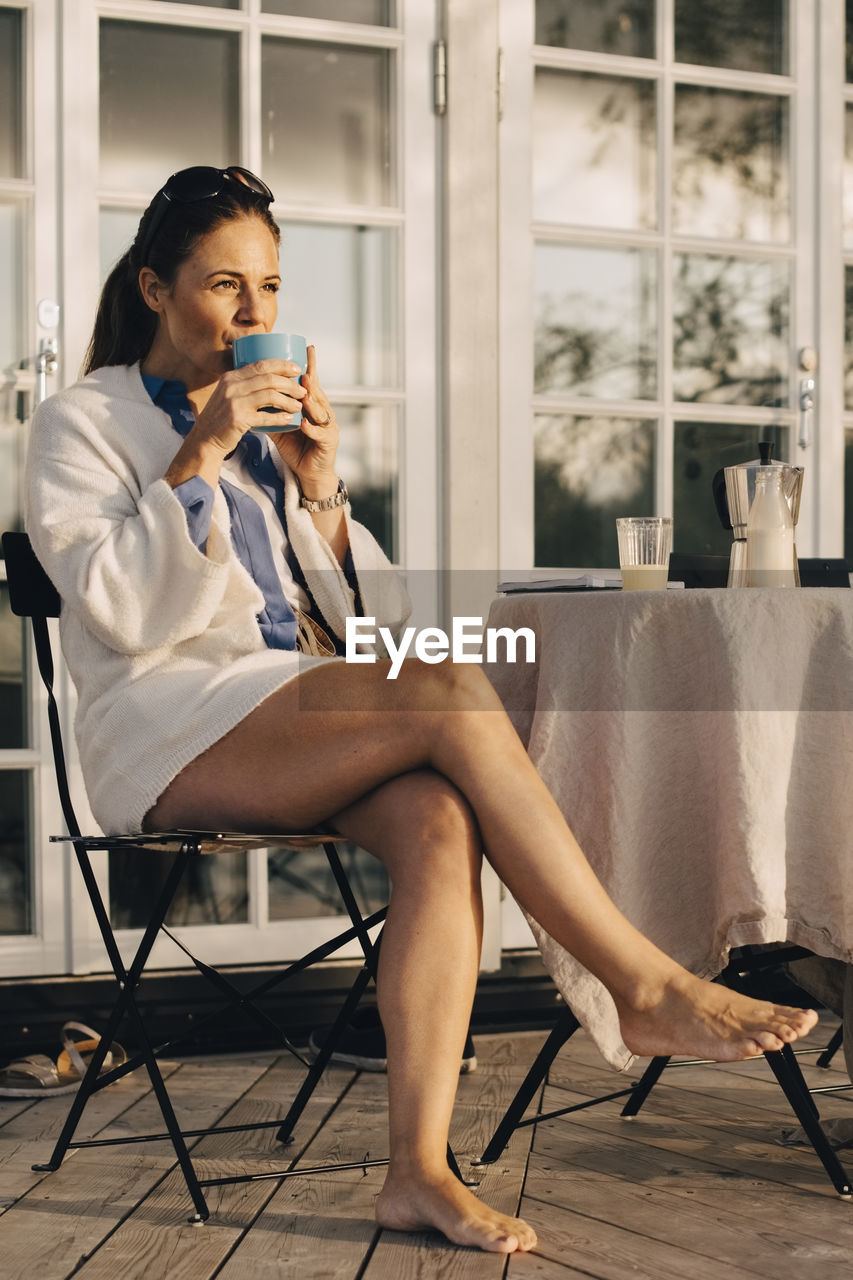 Low angle view of mature woman drinking coffee while sitting at patio in holiday villa