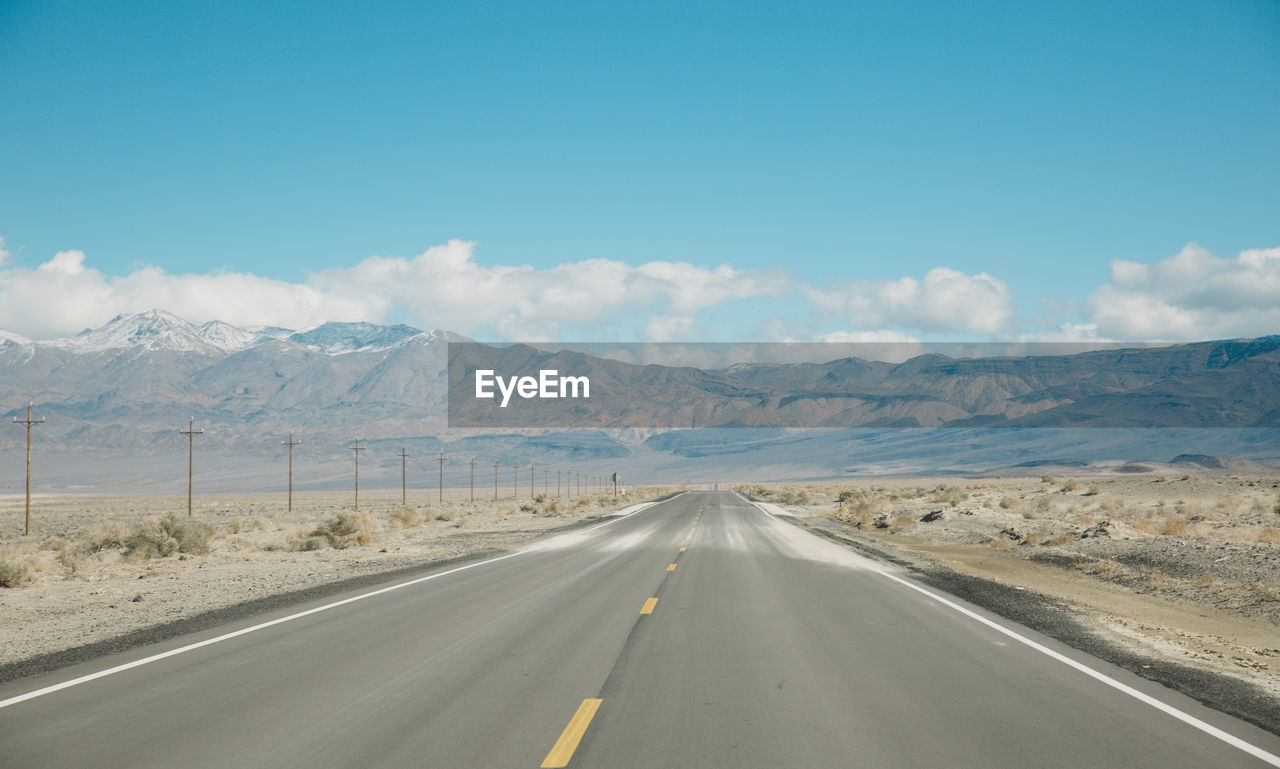 Empty road by mountains against sky