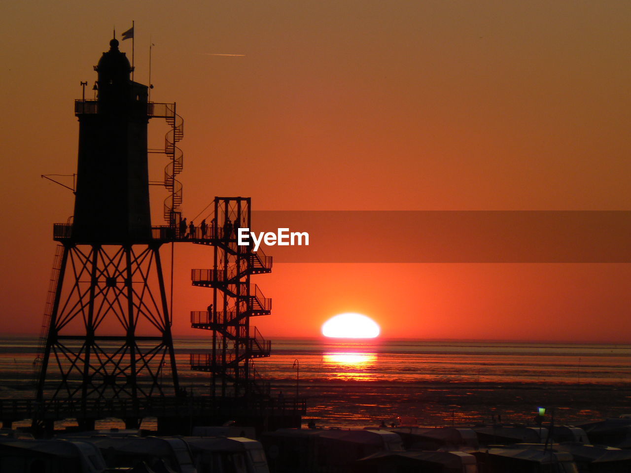 Silhouette lighthouse by sea against orange sky