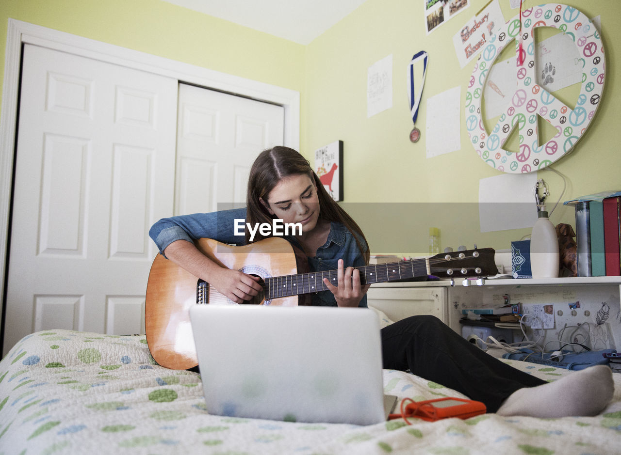 Woman practicing guitar while sitting by laptop at home
