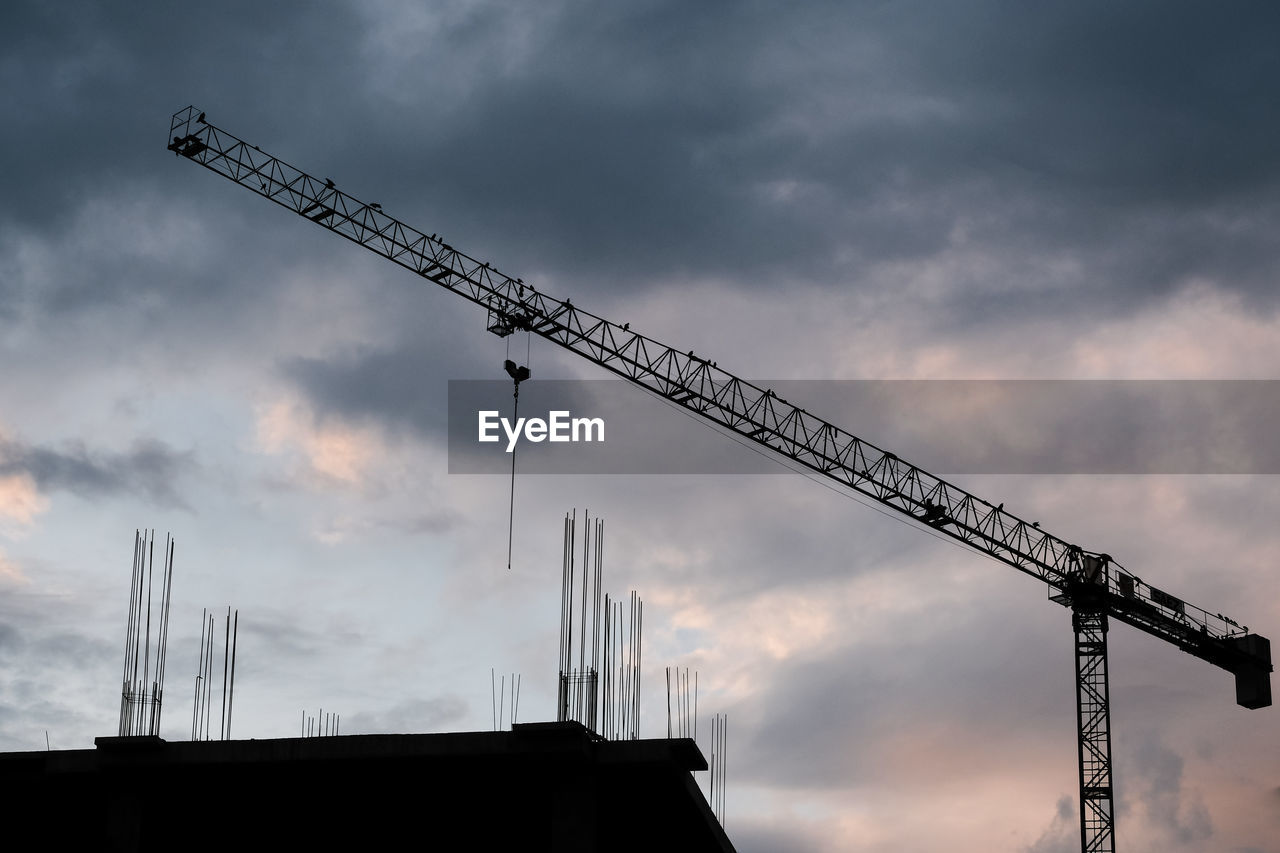 Low angle view of silhouette cranes against sky at sunset