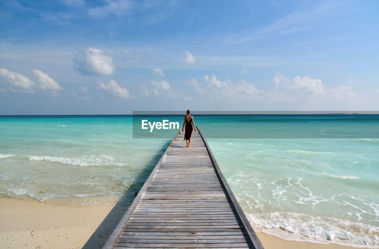 Rear view of woman walking on pier at turquoise sea against sky