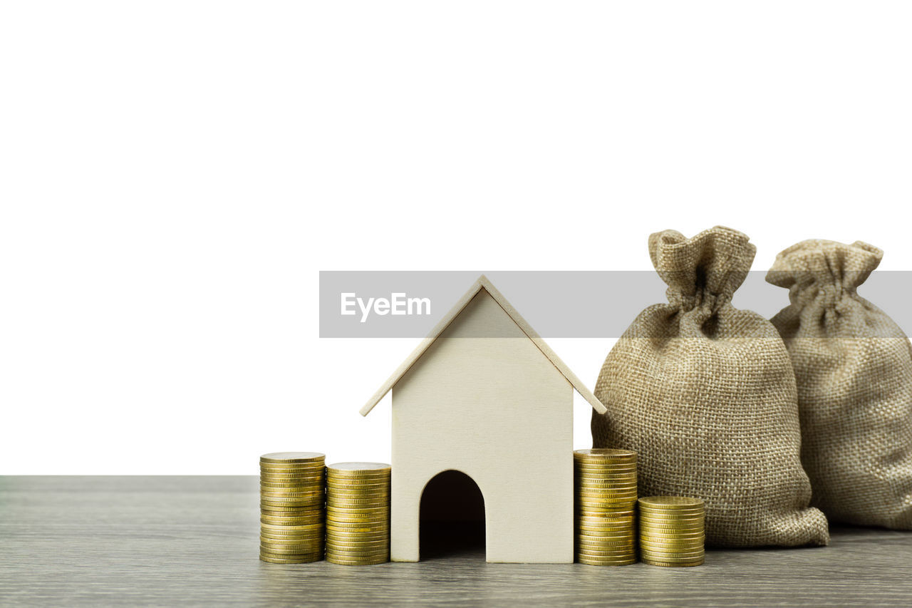 Stacked coins and sacks with model home against white background