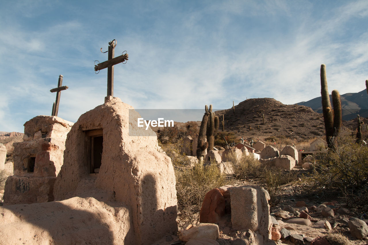 Cross on tombstones at cemetery against sky