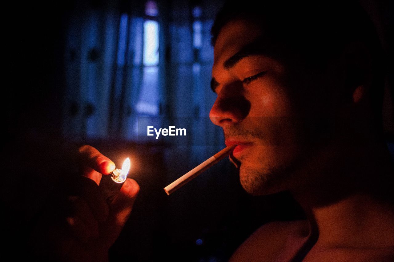 Close-up of young woman smoking cigarette in darkroom