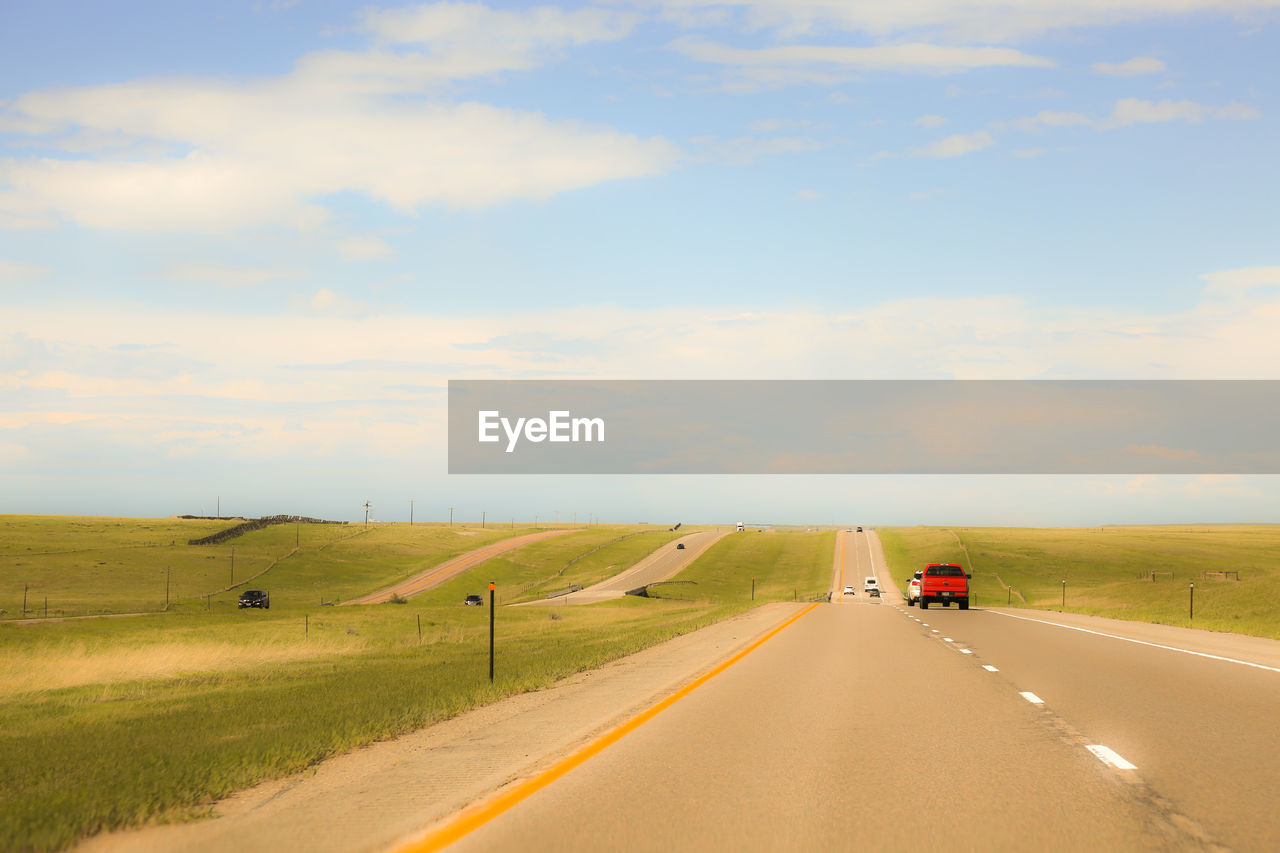 Cars on road by fields against sky