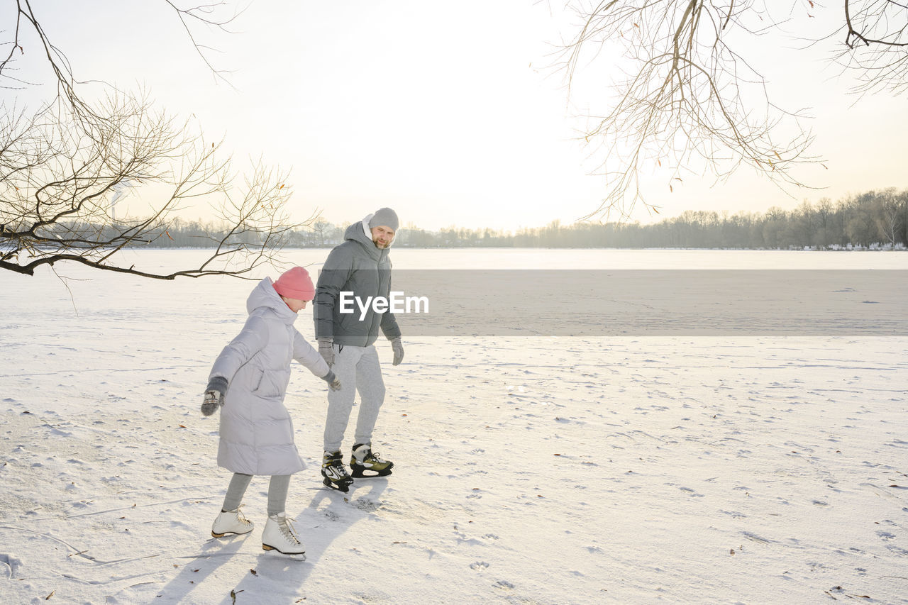 Father and daughter doing ice skating on frozen lake in winter