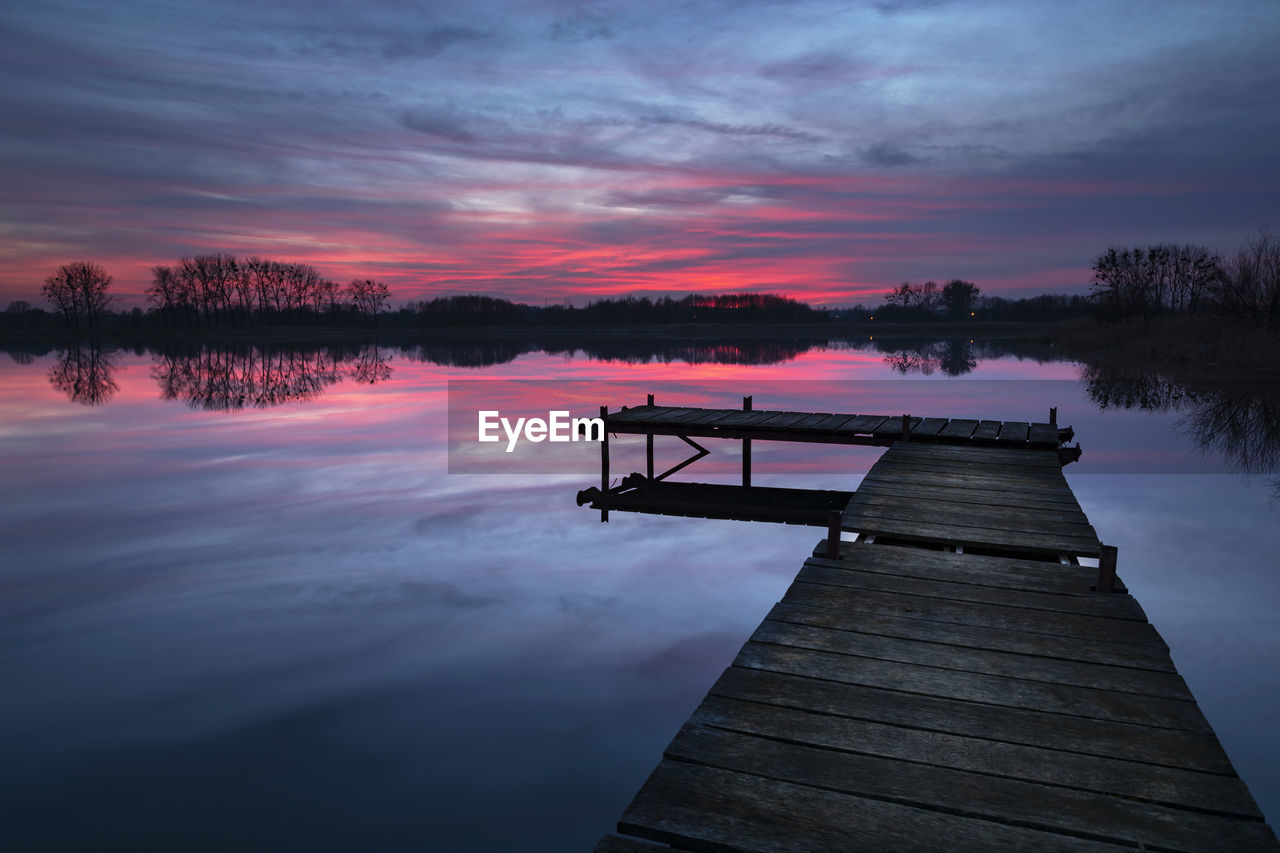 Sunset with dramatic clouds, lake and wooden jetty