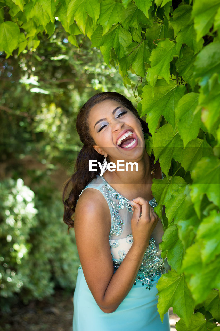 Cheerful young woman standing by plants in park