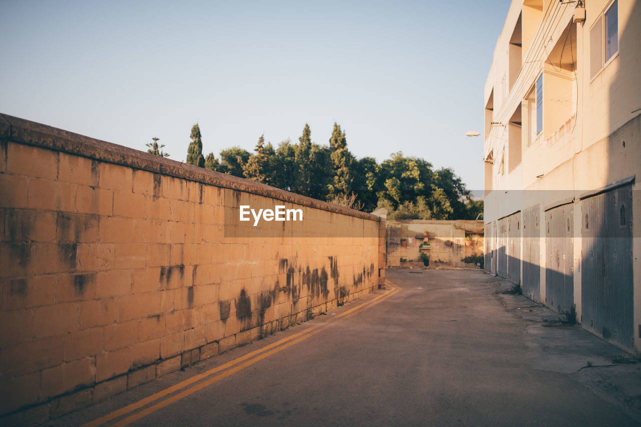 EMPTY STREET AMIDST BUILDINGS AGAINST SKY