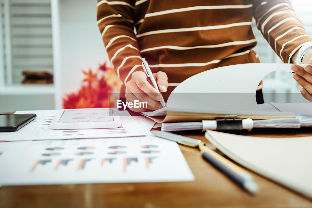 Midsection of businesswoman analyzing reports on desk in office