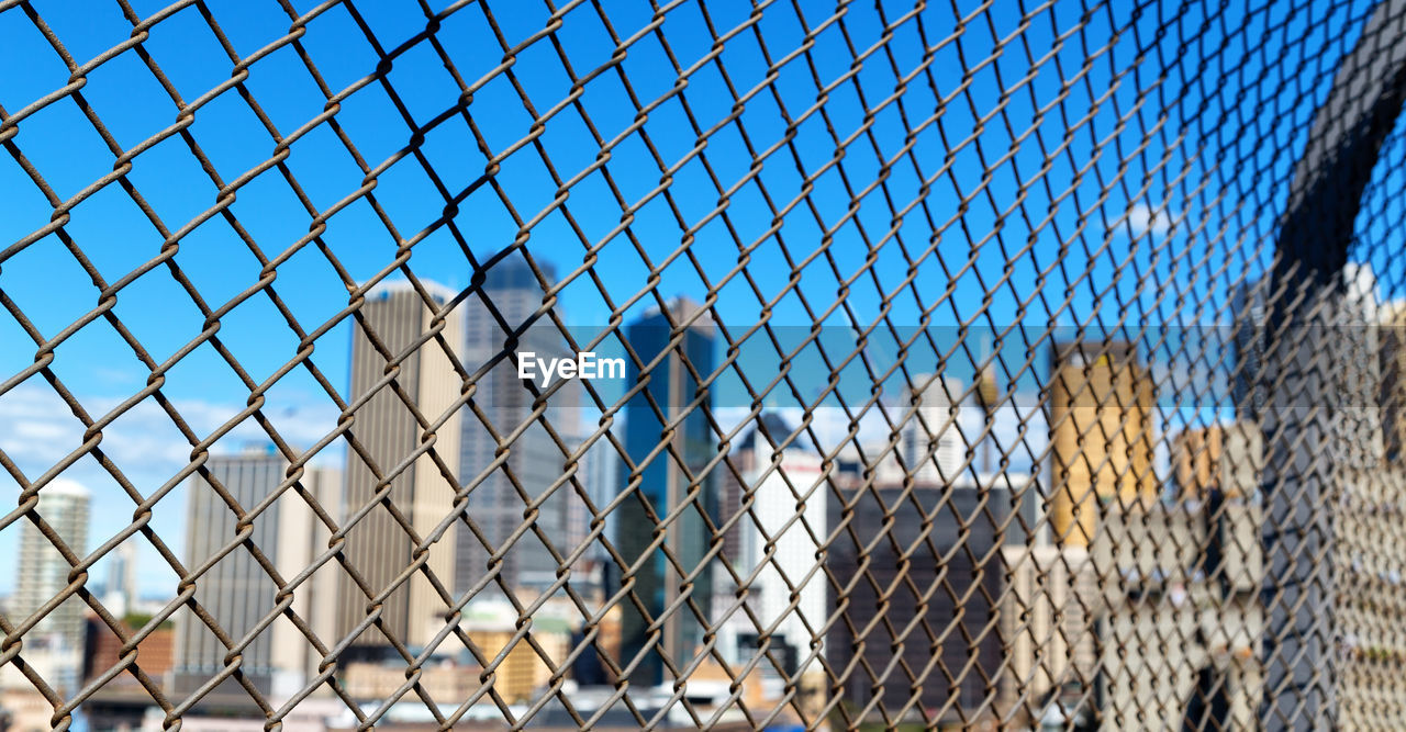 CHAINLINK FENCE AGAINST CLEAR BLUE SKY SEEN THROUGH METAL GRATE