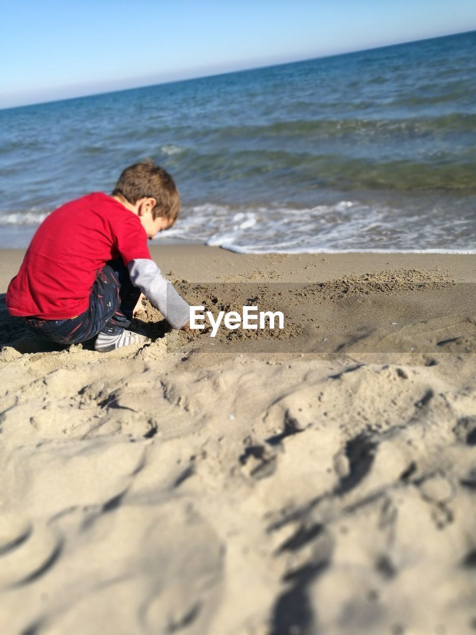 Side view of boy crouching at beach against sky