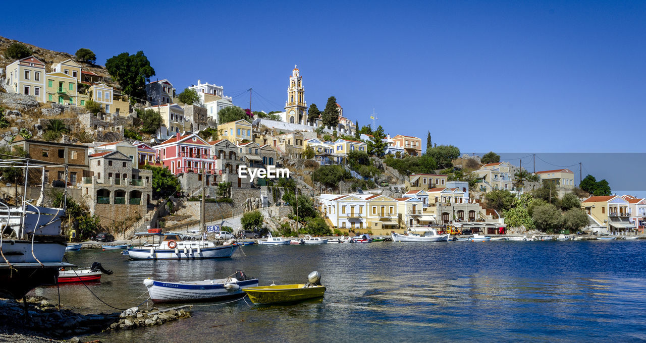 SAILBOATS IN SEA BY TOWNSCAPE AGAINST SKY