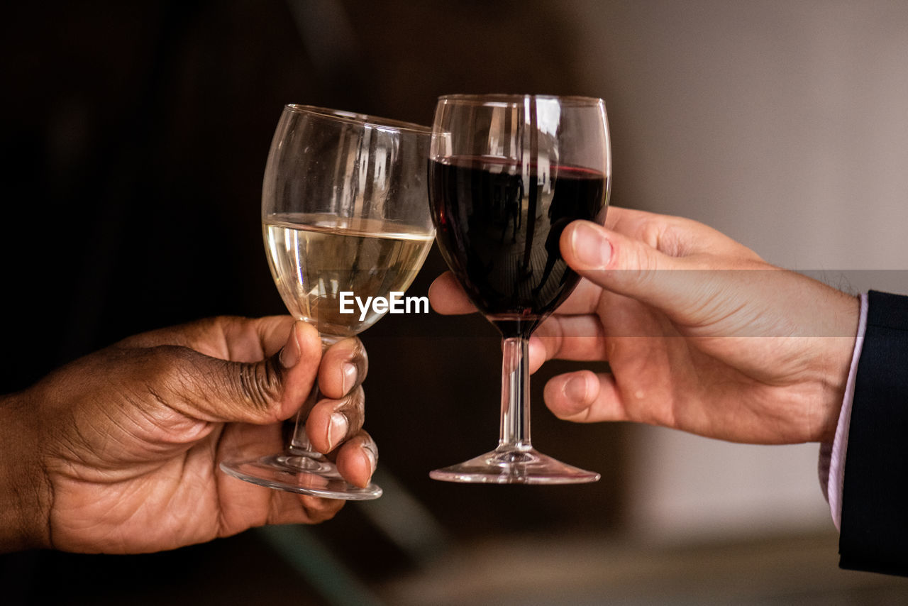 Hands of a black and a white person toasting with glasses of red and white wine