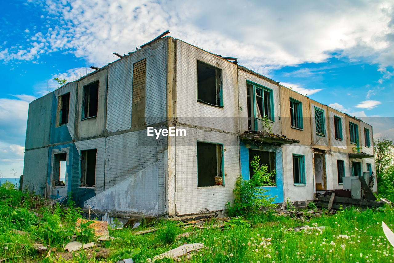 View of an old brick dilapidated building without a roof on green grass against a blue cloudy sky