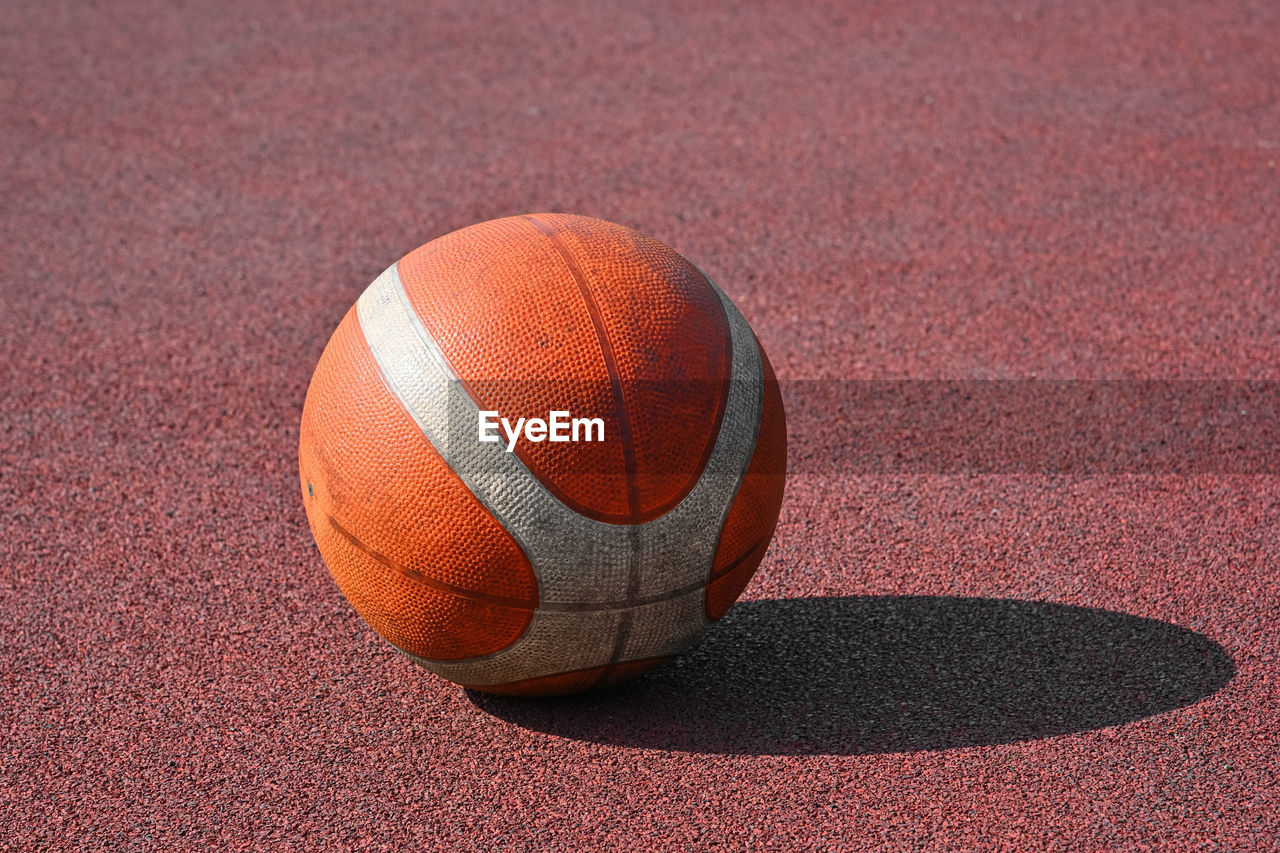 Close up one orange colored unbranded basketball ball over red outdoors court background
