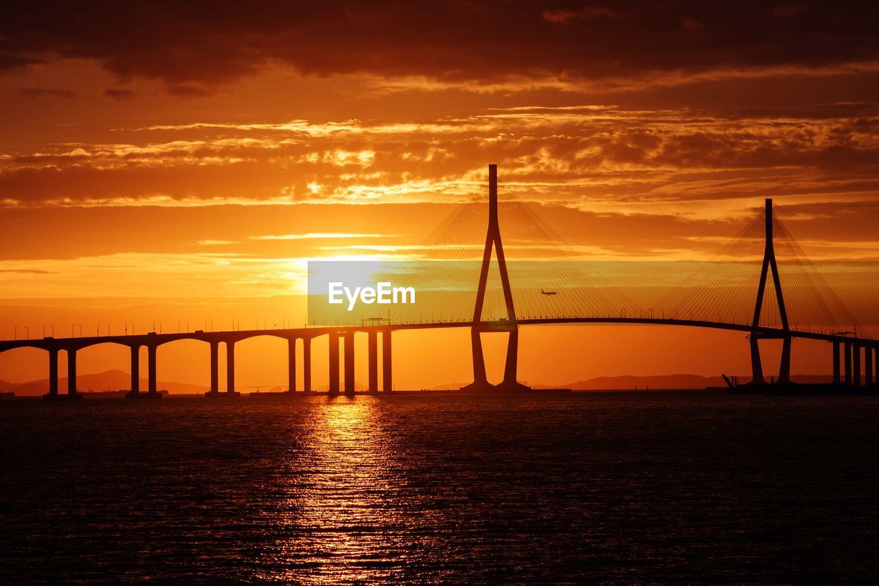 Silhouette bridge over river against orange sky