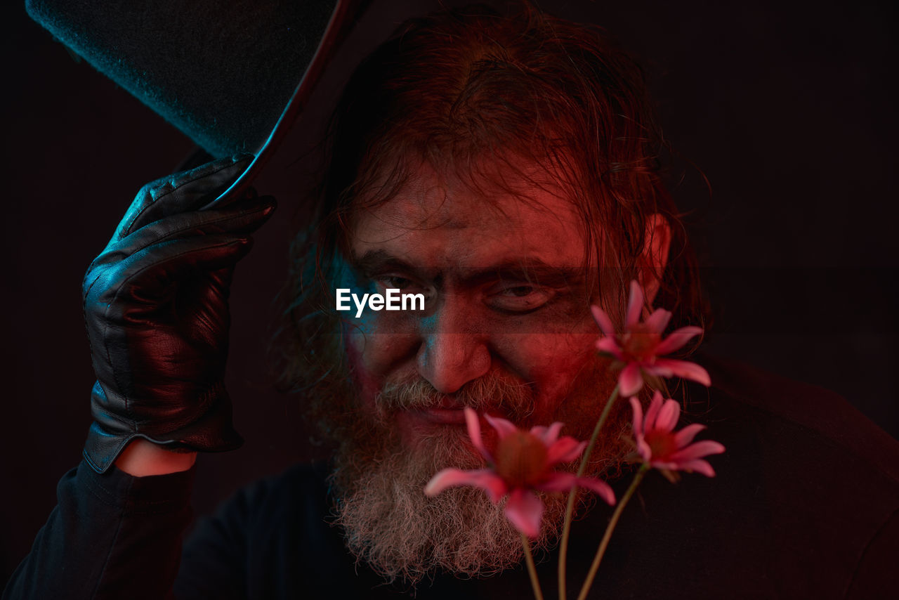 one person, portrait, adult, headshot, facial hair, darkness, black background, red, beard, flower, studio shot, men, indoors, redhead, emotion, human face, flowering plant, looking at camera, person, close-up, plant, nature, beauty in nature