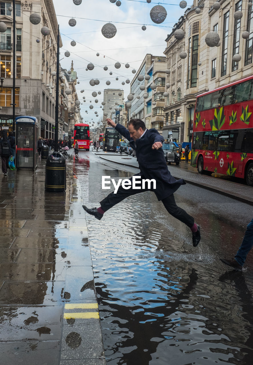 REFLECTION OF MAN IN PUDDLE ON WET STREET