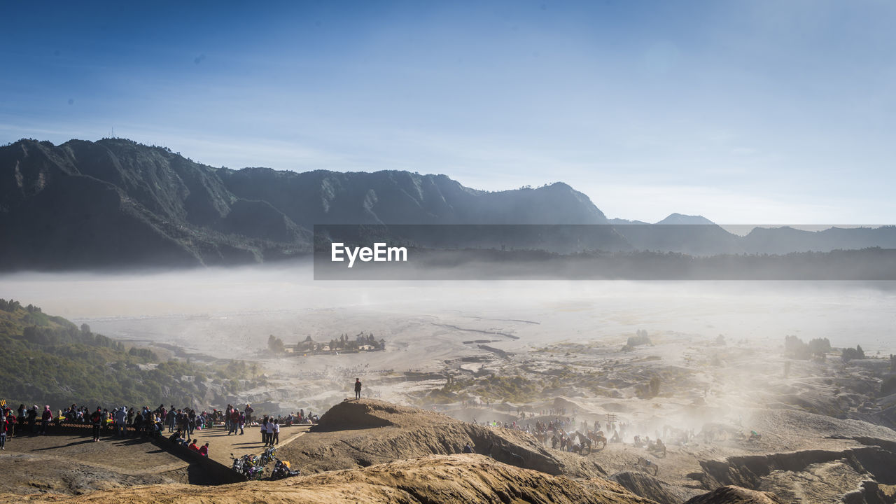 Group of people on landscape against mountain range during foggy weather